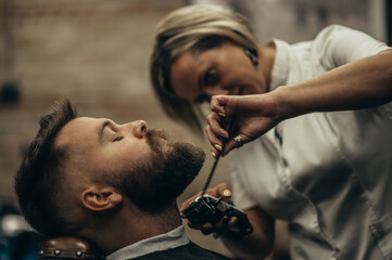 Young bearded man getting beard haircut by hairdresser