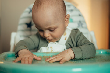 Baby eating with a face stained in food while in a child's dining chair