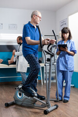 Senior man doing physical activity with electrical bicycle to recover from injury. Patient using...