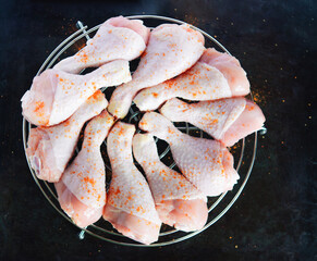 Raw chicken legs with spices on a round metal grill on a dark metal background with space for text. View from above	