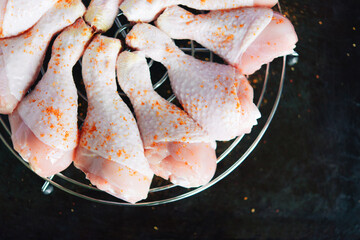 Raw chicken legs with spices on a round metal grill on a dark metal background with space for text. View from above	