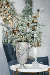 A beautiful Christmas composition of fir branches with Christmas tree toys on them in a classic silver vase on the table