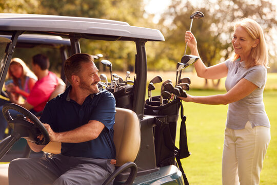 Mature And Mid Adult Couples In Buggies Playing Round On Golf Together