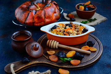 Rice porridge with dried fruits, raisins and honey, baked in a pumpkin on a dark background. Close- up
