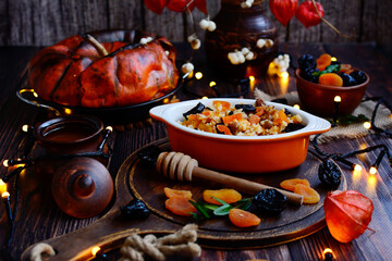 Porridge made of rice, prunes, raisins and dried apricots cooked in a pumpkin on a wooden background with burning garlands