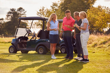 Mature And Mid Adult Couples Standing By Golf Buggy Checking Score Cards Together