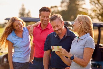 Mature And Mid Adult Couples Standing By Golf Buggy Checking Score Cards Together