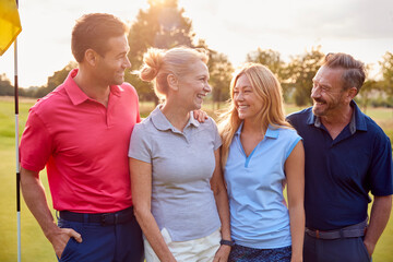 Mature And Mid Adult Couples Standing By Flag On Green Playing Round Of Golf Together