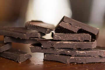Broken pieces of dark chocolate on a wooden brown background.	