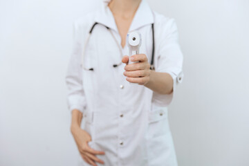 Temperature measurement gun in doctor hands. Close-up shot of doctor wearing protective surgical mask ready to use infrared isometric thermometer gun to check body temperature for virus symptoms.