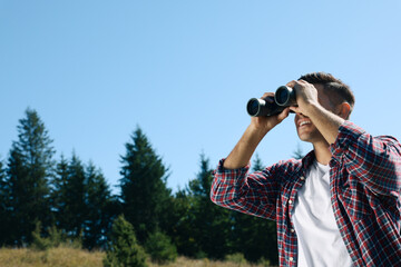 Fototapeta na wymiar Man looking through binoculars outdoors on sunny day