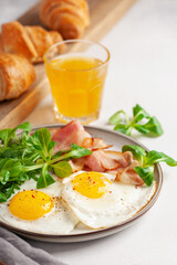 Fototapeta premium Continental breakfast - fried eggs, bacon and lettuce leaves in a plate on a bright background. Top View