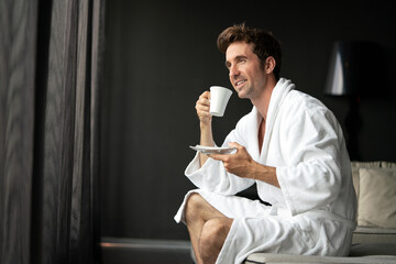 Young handsome man drinking morning coffee in bathrobe - obrazy, fototapety, plakaty