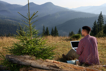 Man working on laptop outdoors surrounded by beautiful nature, back view