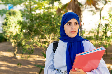 Smiling young Muslim woman in hijab holding a folder going to the university