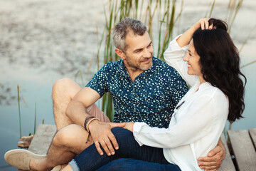 A mature married couple are sitting by the lake and hugging. happy lovers 50 years old