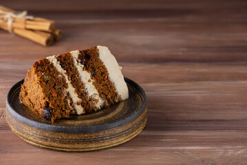 Piece of homemade vegan carrot cake with coconut cream and nuts on a wooden table. Sugar, gluten and lactose free. Horizontal orientation, copy space.