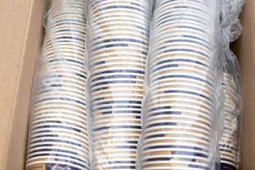lot of paper cups in a row one over another in cellophane pack in a cardboard brown box.stack of cups for coffee machine. tea, americano, espresso, cappuccino, hot chocolate.coffee business paper eco 