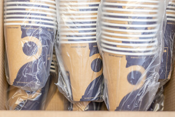 lot of paper cups in a row one over another in cellophane pack in a cardboard brown box.stack of cups for coffee machine. tea, americano, espresso, cappuccino, hot chocolate.coffee business paper eco 