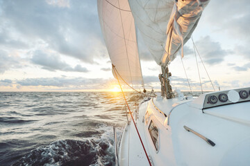 Yacht sailing in an open sea at sunset. Close-up view of the deck, mast and sails. Clear sky after...