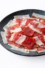 Spanish serrano ham slice on black plate isolated on white background