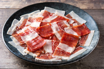 Spanish serrano ham slices on black plate on wooden table