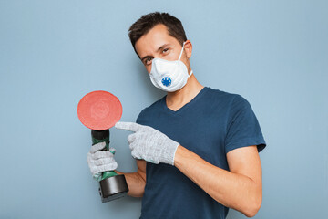Young handyman wearing respirator grinding wall with disc sanding machine. Worker labor and...