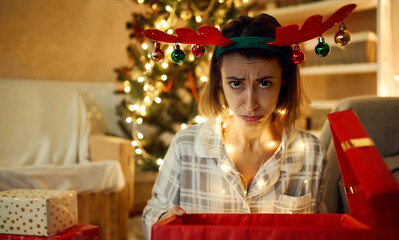 Close up funny frowns face of festive x-mas woman. Disappointed woman with opened bad Christmas gift box at home