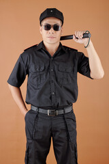 Fototapeta na wymiar Serious confident police office in black uniform and sunglasses holding baton and looking at camera