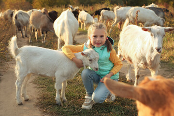 Naklejka premium Farm animal. Cute little girl hugging goatling on pasture