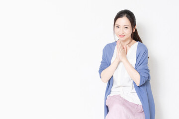 白い壁の前の椅子に座ってお願いのポーズをする主婦