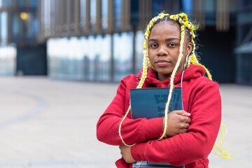 portrait of serious sad african american girl near college. black student with book at university before exam. young woman with braids, dreadlocks at business center