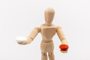 A wooden Gestalta doll or mannequin holds red and white pills in its hands on light background. The concept of choice.