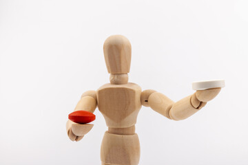 A wooden Gestalta doll or mannequin holds red and white pills in its hands on light background. The concept of choice.