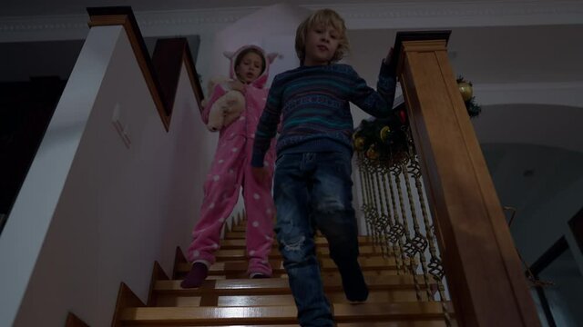 Caucasian boy and girl walking downstairs in slow motion talking. Positive little brother and sister at home indoors in the morning. Lifestyle and childhood concept