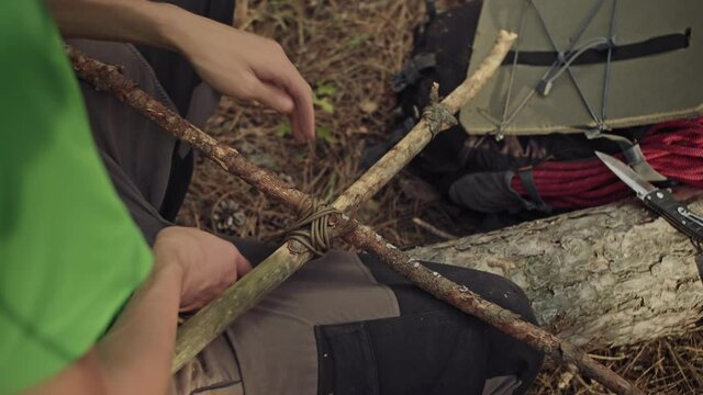 A male survivalist ties sticks. Survival in the forest. A man builds a shelter in the forest