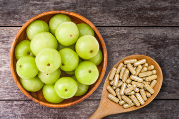 Close-up fresh organic green Amla or Indian Indian Indian gooseberry fruits (amla, phyllanthus emblica ) with capsules isolated on rustic wood table background. Overhead view. Flat lay.