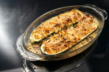 Baked zucchini filled with vegetables, feta cheese and parmesan in a glass casserole fresh from the oven, dark background with copy space, selected focus