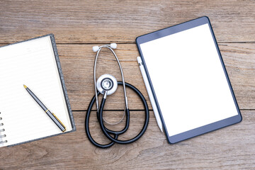Mock up blank screen digital tablet with medical stethoscope and empty notebook and pen on wood...