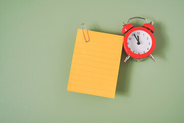 blank yellow note paper with line and red analog alarm clock on green background  with copy space,...