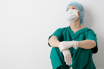 Tired nurse in scrubs and protective mask sitting on the floor in clinic corridor and resting after...
