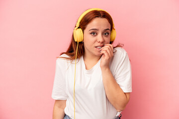 Young caucasian woman listening to music isolated on pink background biting fingernails, nervous and very anxious.