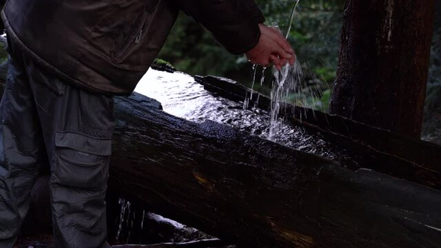 A man washes his hands on a forest wooden trough - (4K)
