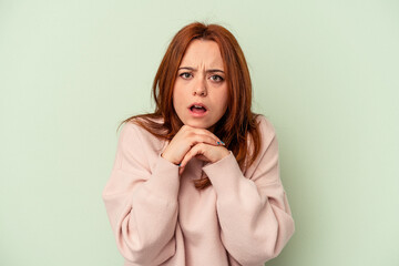 Young caucasian woman isolated on green background praying for luck, amazed and opening mouth looking to front.