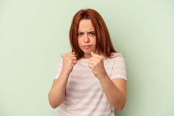 Young caucasian woman isolated on green background showing fist to camera, aggressive facial expression.