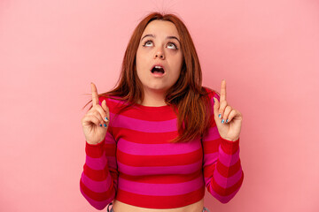 Young caucasian woman isolated on pink background pointing upside with opened mouth.