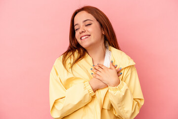 Young caucasian woman isolated on pink background laughing keeping hands on heart, concept of happiness.
