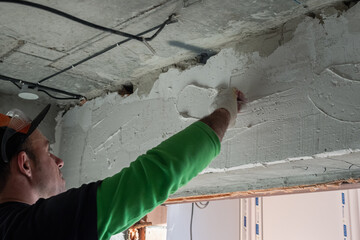 A construction worker plastering a wall with a small trowel. Back view. Interior finishing concept.