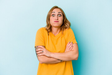 Young caucasian woman isolated on blue background blows cheeks, has tired expression. Facial...