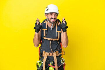 Young caucasian rock climber man isolated on yellow background with fingers crossing